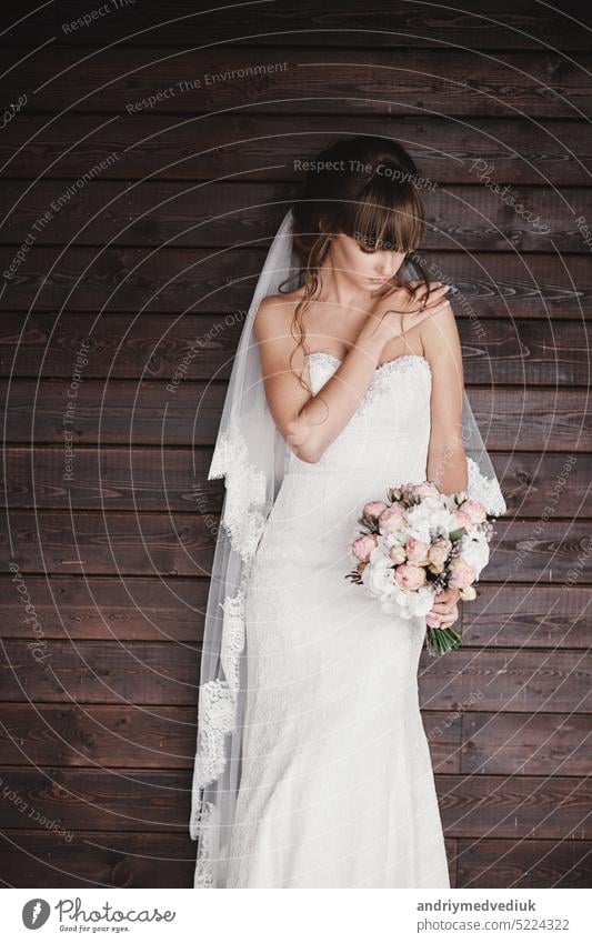 beautiful young bride in a luxury white dress with a bouquet in her hand on a wooden background outdoors bridal style girl elegance portrait makeup copy space