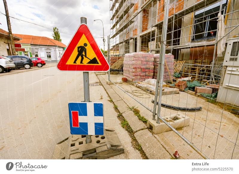 Traffic road signs placed on the street next to fenced undone edifice. Prohibited enter at construction zone, work in progress Approach Area Attention Barricade