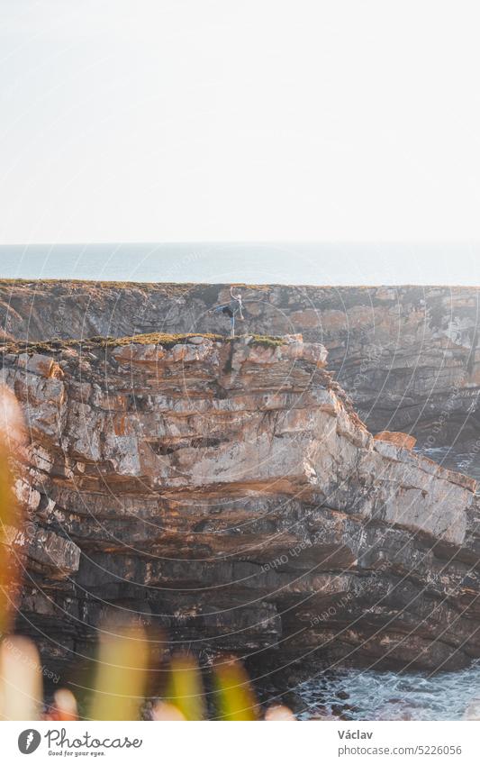 Hiker celebrates its success. Breathtaking cliffs with pebble beach in the afternoon sun on the Atlantic coast at Vila Nova de Milfontes, Odemira, Portugal. In the footsteps of Rota Vicentina