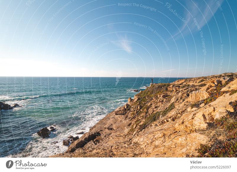 Hiker enjoys the breathtaking cliffs with a pebble beach in the afternoon sun on the Atlantic coast at Vila Nova de Milfontes, Odemira, Portugal. In the footsteps of Rota Vicentina. Fisherman trail