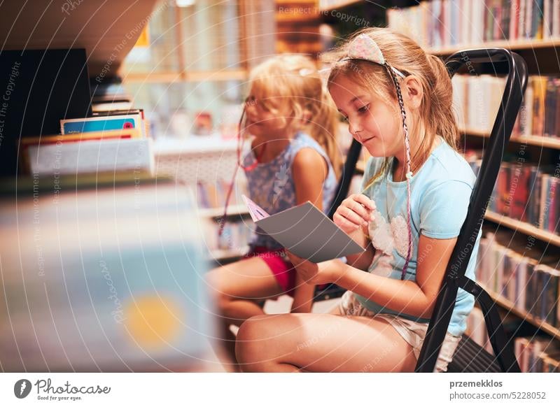 Schoolgirls looking for books in school library. Students choosing set books. Elementary education. Doing homework. Back to school back schoolgirl child reading