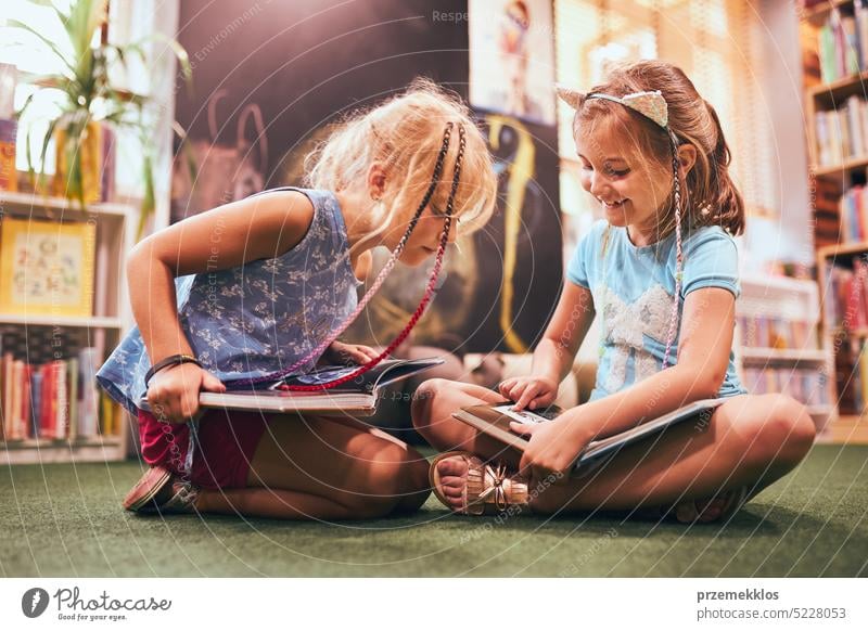 Two primary schoolgirls doing homework in school library. Students learning from books. Pupils having fun in library. Back to school back student studying child