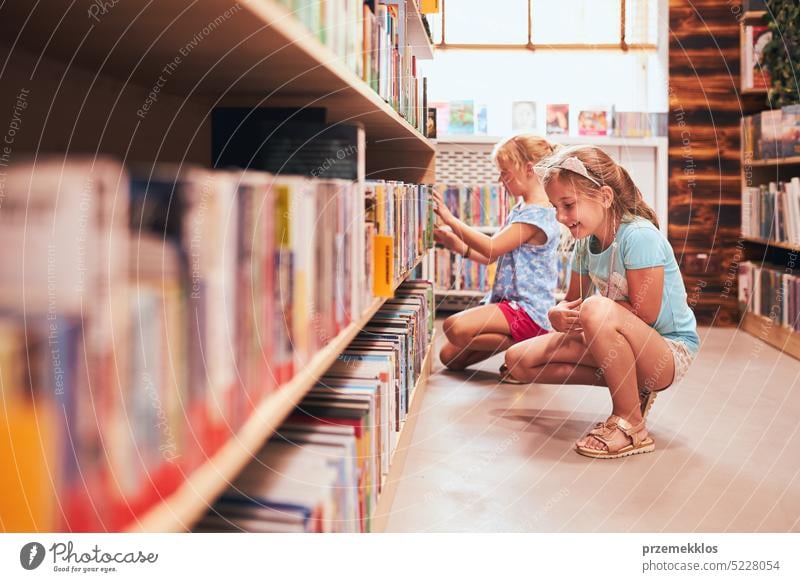 Two schoolgirls choosing books in school library. Primary school students learning from books. Children having fun in school club. Back to school back