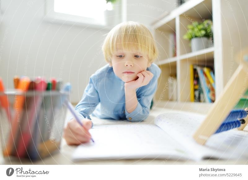 Elementary student boy doing homework on floor at home. Child learning to count, solves arithmetic examples in workbook. Math tutorial. Preparing preschooler baby for school.