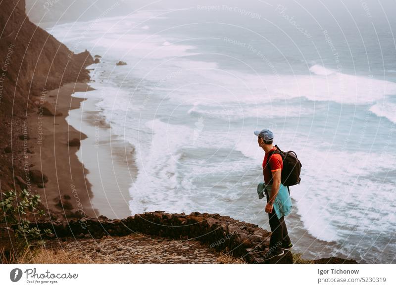 Tourist walking long way along cliff coastline with ocean waves from Cruzinha to to Ponta do Sol. Huge mountains on the trekking path. Santo Antao Island, Cape Verde