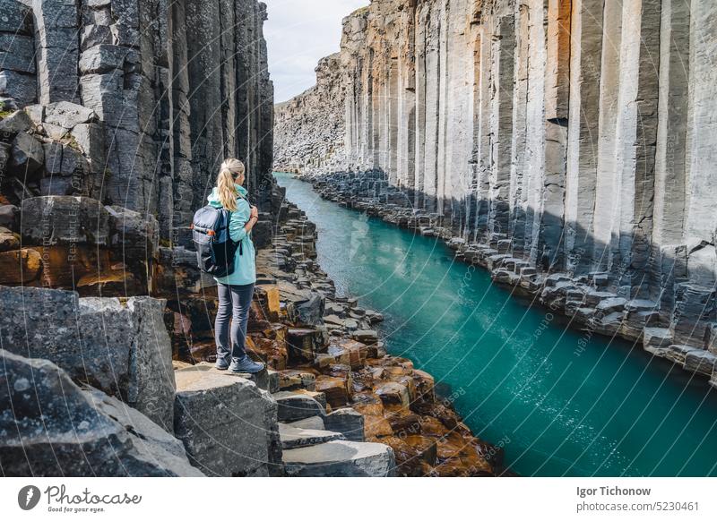 Woman hiker with backpack enjoying Studlagil Canyon. Unique Jokulsa basalt colums and A Bru river. Spectacular outdoor scene of Iceland, Europe. Beauty of nature concept background