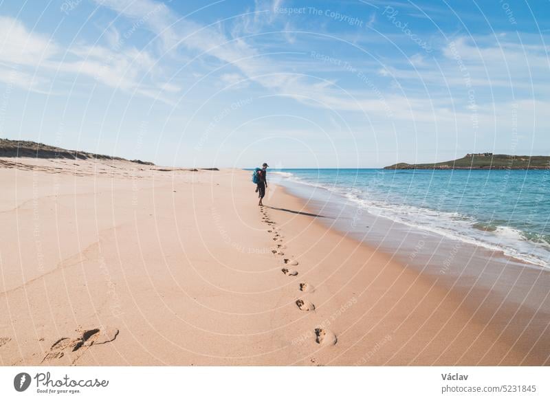 Passionate backpacker, backpack and boots in hand, walks along the Praia da Ilha do Pessegueiro beach on the Atlantic Ocean near Porto Covo, Portugal. In the footsteps of Rota Vicentina