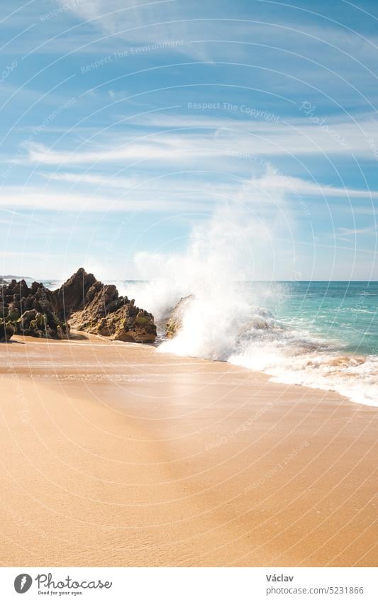 Waves of the Atlantic Ocean on a sunny day crashing against a rock on the sandy beach of Praia da Ilha do Pessegueiro near Porto Covo, western Portugal. Rota Vicentina