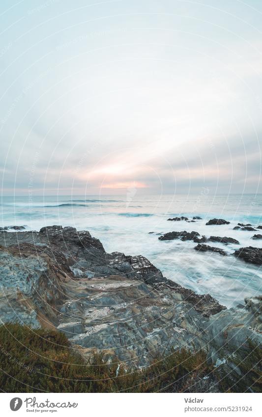 Stormy Atlantic Ocean shows its power with waves crashing into the rocks at sunset off Porto Covo, Portugal. The beauty of the Fisherman Trail, Rota Vicentina