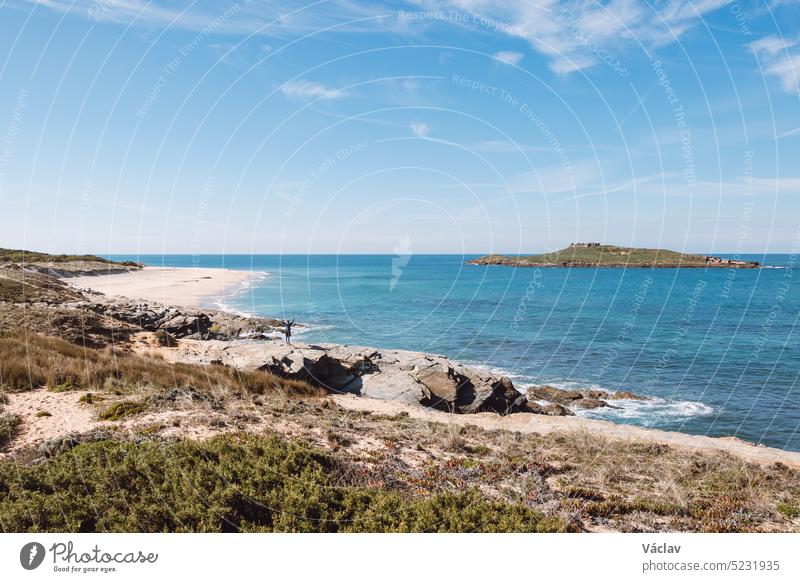 Man wearing sports clothes and carrying a backpack takes pictures of the Atlantic coastline near Porto Covo, Portugal. Capturing moments on a mobile phone