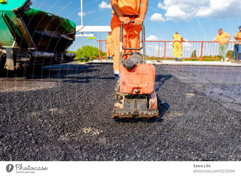 Worker compacts tarmac using vibration plate compactor Alignment Asphalt Asphalting Bitumen Blacktop Blacktopping Bridge Building Site Compact Compacting