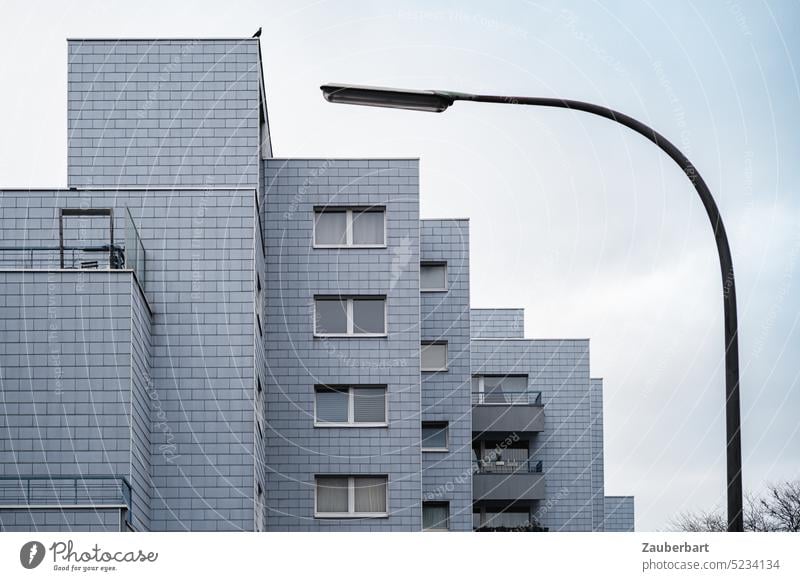 Rather the blackbird on the roof ... gray apartment house in stepped architecture, harmoniously framed by arched street lamp Apartment Building Apartment house