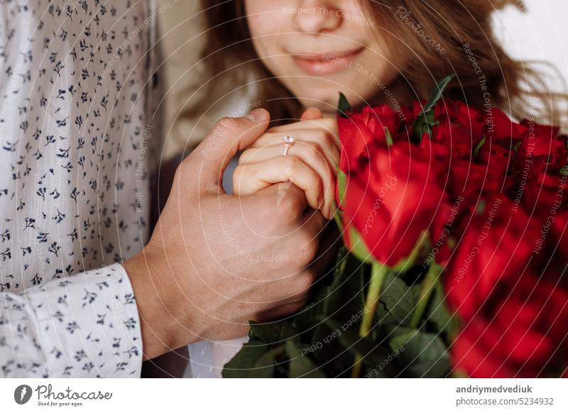 young man holding his fiance's hand with gold ring while making a marriage proposal with bouquet of red roses. Engagement of a young couple in love. The concept of love and togetherness.