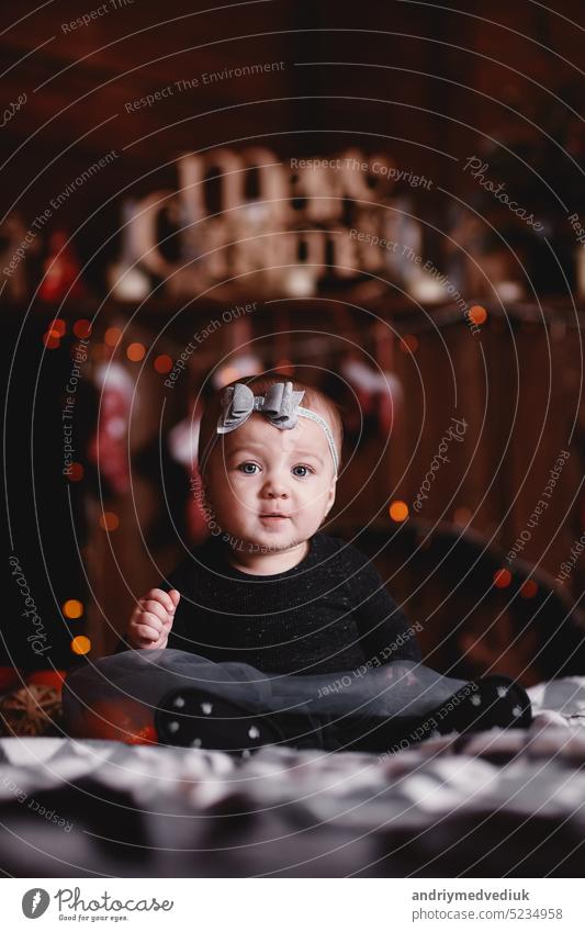 cute baby girl in dress and bow on head on bed with Christmas background behind. christmas tree white winter portrait kid home happy happiness family beautiful