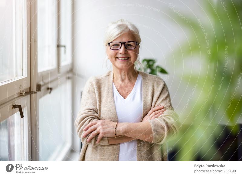 Portrait of smiling senior businesswoman standing with arms crossed in office real people indoors loft window home mature adult one person attractive successful