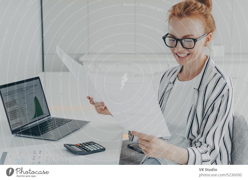 Glad European female financier studies financial graphs diagrams counts expenses holds papers graphics document woman business computer internet technology