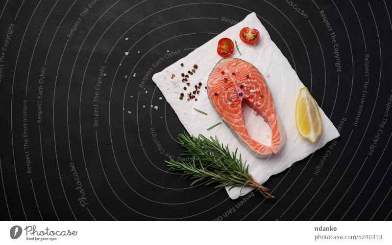 Raw salmon steak on a white board, lemon slices, spices. Top view on black table raw fish food piece fresh background seafood fillet healthy red gourmet