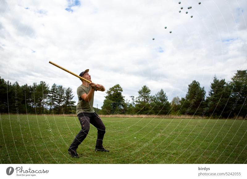 Young man tries to hit away approaching golf balls Man Golf balls action repulse sb./sth. Hit balls Many playground excessive demands vindicate too many defense