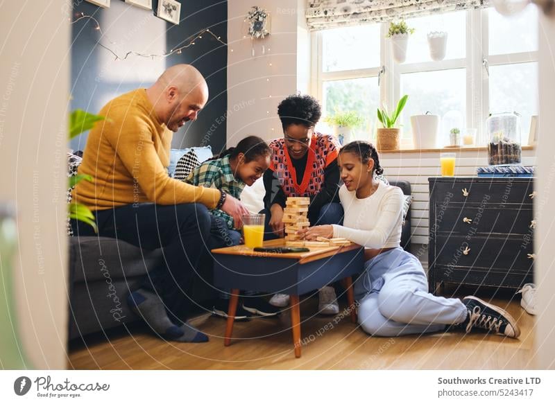 Family at home playing board game, boy with down syndrome family multiracial lifestyle father mother smile cheerful happy girl togetherness leisure fun son