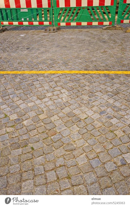 green plastic warning beacons with red-white stripes and a yellow line on a cobblestone road / road construction measure Road construction