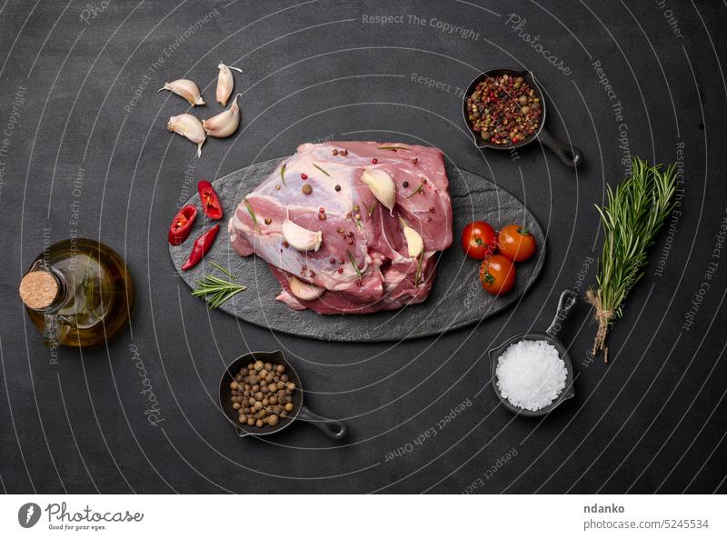 A piece of pork ham on a black board and spices olive oil, salt, rosemary branch and pepper garlic food slice butcher ingredient sirloin meal bottle raw part