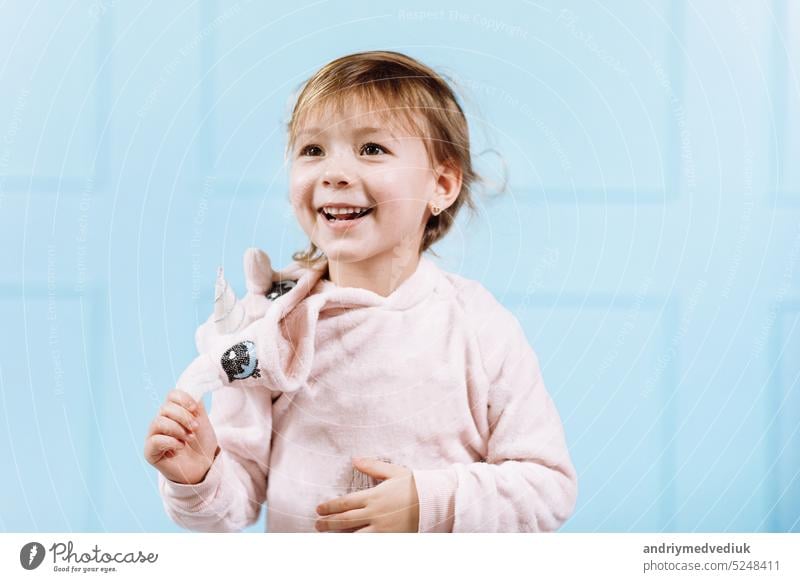 Smiling beautiful little girl in unicorn pink costume is smiling and having fun on a blue wall background. happy childhood hat face cute kid adorable smile