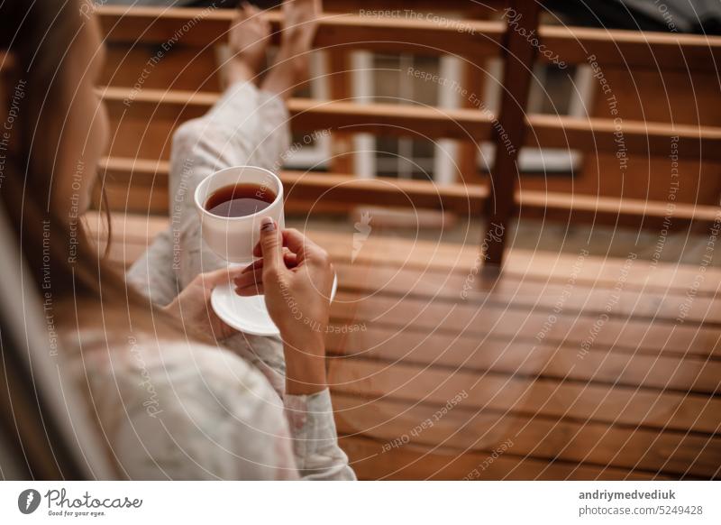 Young female standing after taking a shower in the morning on balcony of the hotel. holding a cup of coffee or tea in her hands. Looking outside nature forest and Mountain