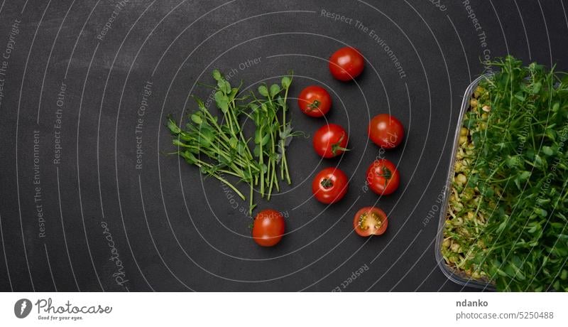 Red tomato and sprouted pea seeds on a black background, microgreens for salad, detox. Top view raw red root pepper plant seedling small studio table top vegan