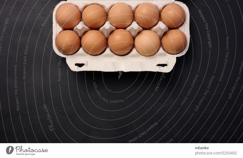 Raw brown chicken eggs in a paper cardboard container on a black background, top view eggshell raw ten box breakfast uncooked farm food fragile nutrition carton