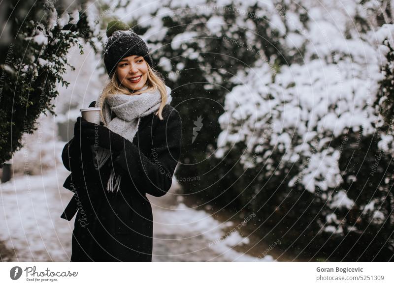 Young woman in warm clothes enjoying in snow with takeaway coffee cup adult air alone beautiful beauty brunette cap charming coat cold cute day emotions female