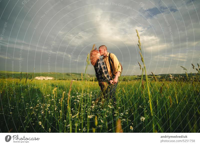 Loving hipster couple walking in the field, kissing and holding hands, hugging, lying in the grass in the summer at sunset. valentines day man love relationship