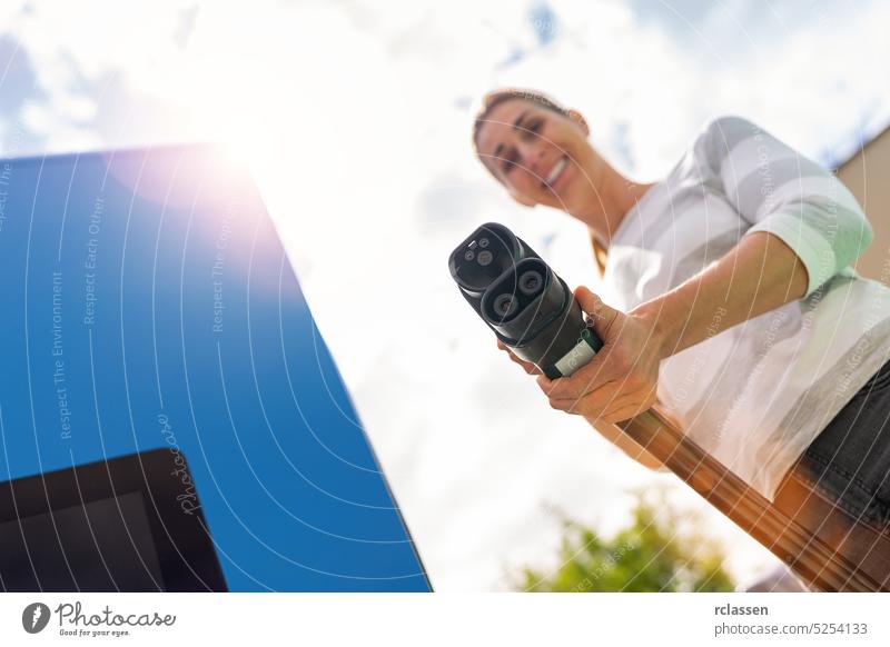 Happy woman holding a DC CCS2 EV charging connector on a 300KW Hypercharger or Supercharger for recharge her car. happy female nfc debit card payment paying