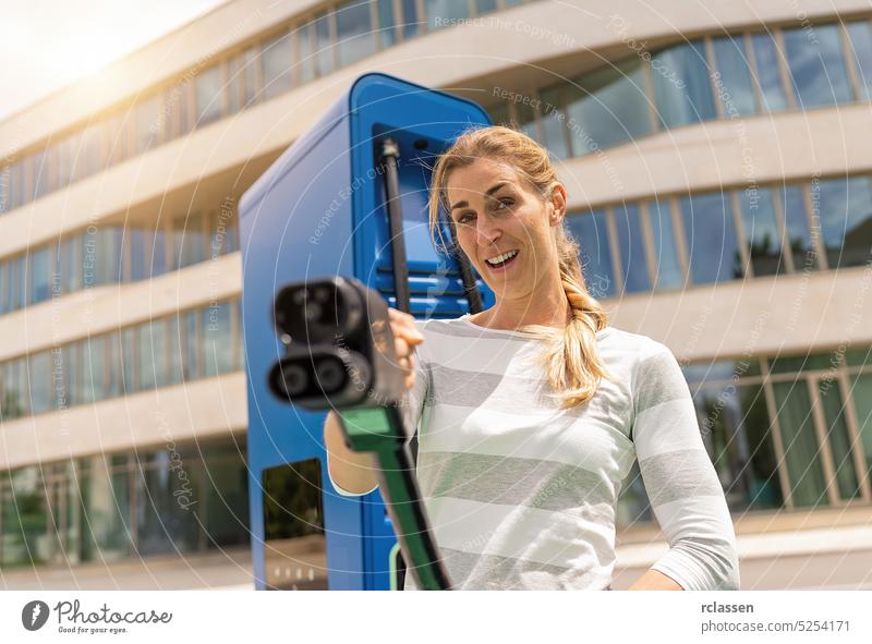 woman holding a DC CCS2 EV charging connector on a Hypercharger or Supercharger for recharge her car. happy female nfc debit card payment paying rfid