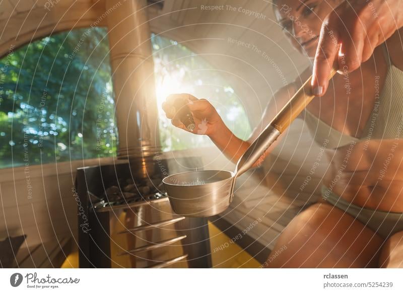 Woman dripping essential aromatic oil from a dropper bottle in to water for a trowel in a wooden barrel sauna in norway. Steam, spa and wellness concept, relaxing and enjoy the holidays