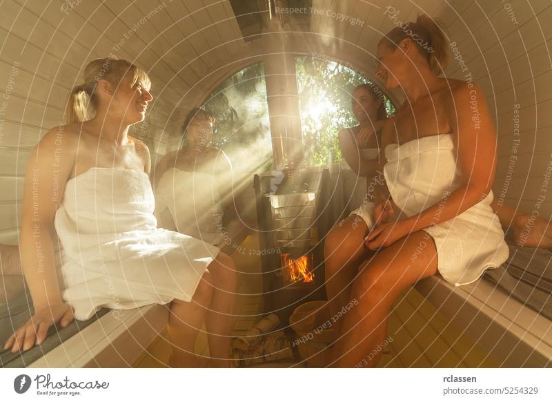 Four girlfriends sitting with towels in a hot wooden barrel sauna at in norway. Are relaxed, laughing and enjoy the holiday while relaxing in the finnish sauna cabin.