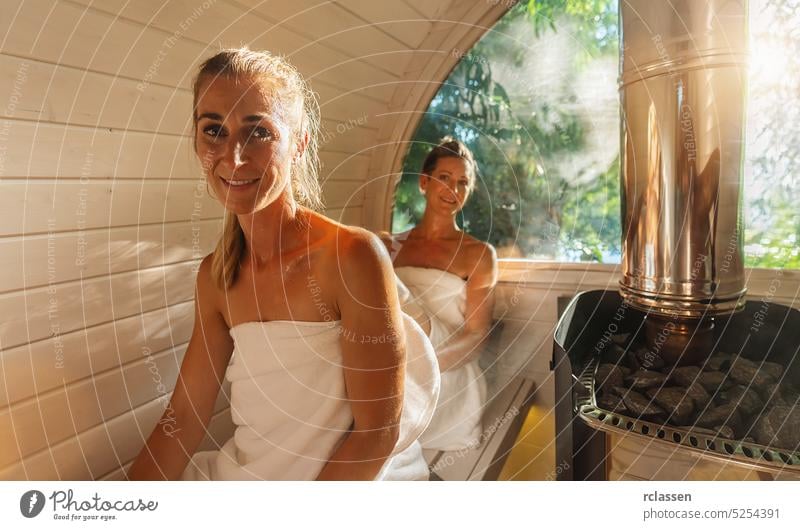 Relaxed woman and her girlfriend at the wooden barrel sauna at Summer in norway. Enjoy holiday while relaxing in the finnish sauna cabin. friends thermal winter