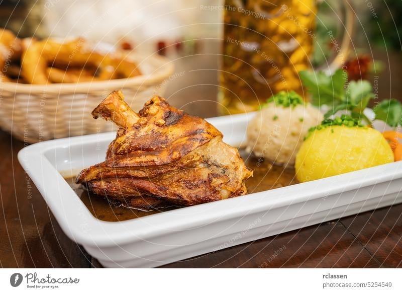 Schweinshaxe, in German cuisine, is a roasted ham hock (or pork knuckle). The ham hock is the end of the pig's leg, with potato dumpling, brezen and beer mug in a Bavarian beer garden or oktoberfest