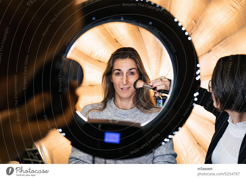 makeup artist powders a models face posing at camera through ring light lamp at a Photo shooting with ring light powder brush led beauty portrait