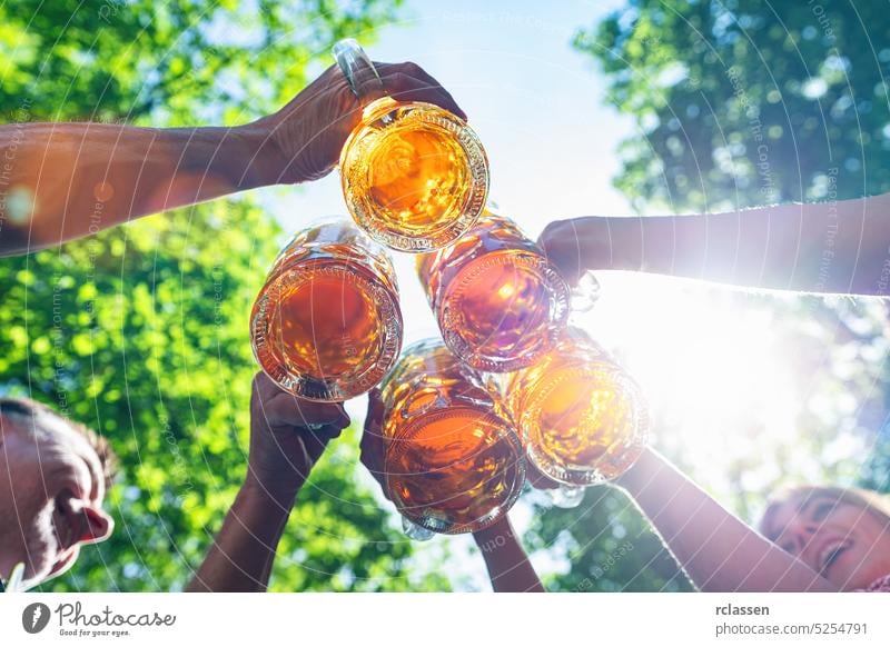 Five friends, men and women, having fun in beer garden clinking glasses with beer in a Beer garden, Munich, Germany tap hands brezen bavarian festival