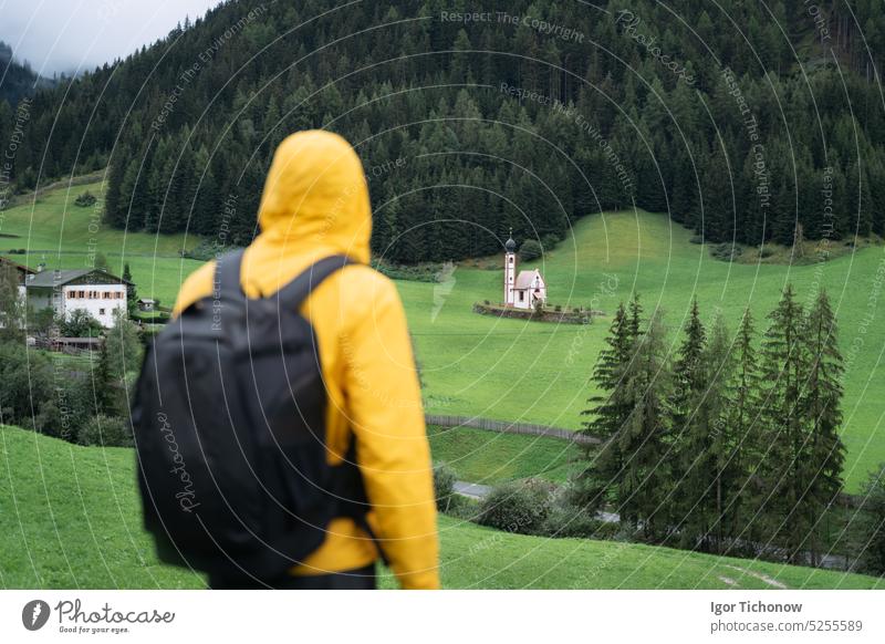 Hiking man with backpack enjoy the view of St. Johann church in Val di Funes valley, Dolomites, Italy, Europe dolomites italy funes village santa male maddalena