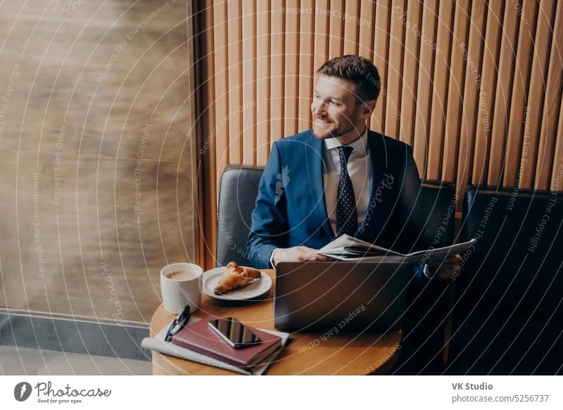 Business man looking outside window in cafe while holding newspaper young elegant laptop businessman reading male chronicle work table unshaven handsome