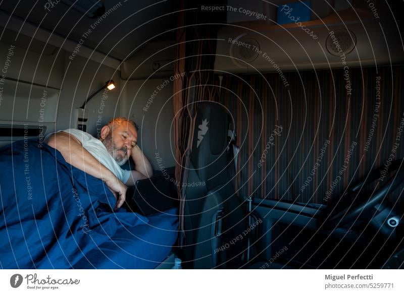 Trucker lying in the bed of the truck, entertained with a tablet, before sleeping. truck driver cabin profession man interior relaxation rest transport overtime