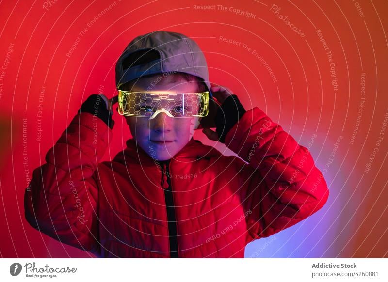 Boy adjusting futuristic digital goggles boy illuminate neon cyberpunk colorful bright modern style glow glasses kid cap coat child vivid eyewear vibrant