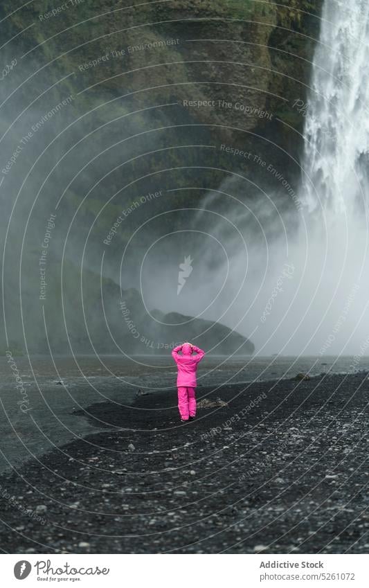 Unrecognizable traveler standing near waterfall woman rocky coast river nature admire landscape iceland europe explore adventure tourism fresh warm clothes