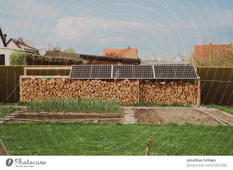 Homegrown vegetables and wood stock with firewood under solar panels in the garden photovoltaics wood supply Wood Firewood sustainability sustainable lifestyle