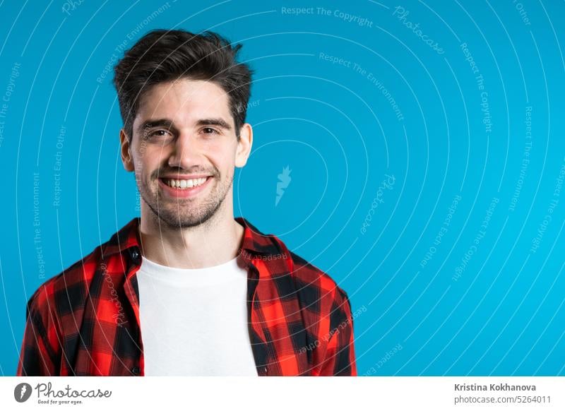 Handsome european man with trendy hairdo in red plaid wear on blue studio background. Copy space. Cheerful guy smiling and looking to camera. person portrait