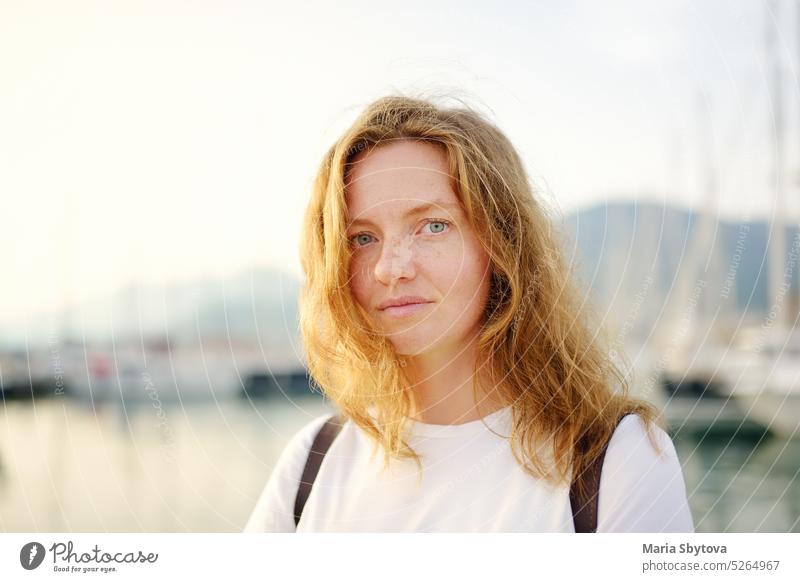 Portrait of charming young tourist woman on the Mediterranean coast. Attractive red-haired girl hiking by the sea shore. Tourism, adventure and travel portrait