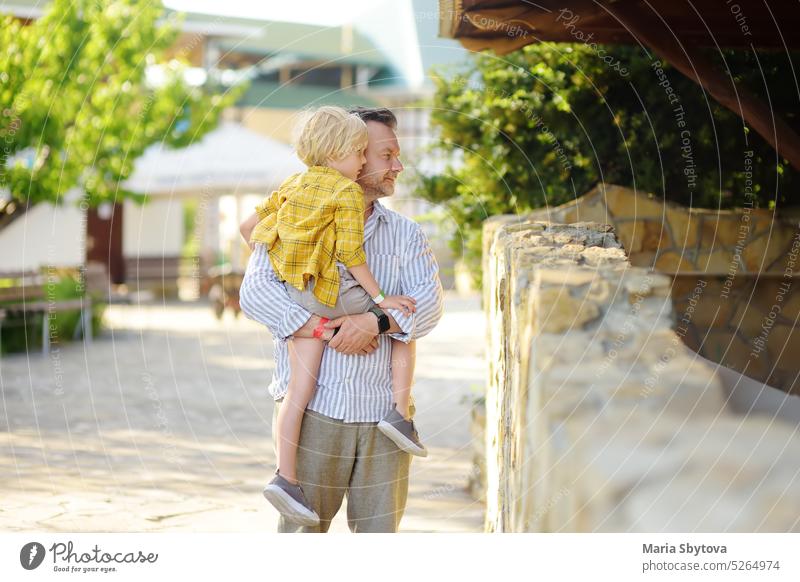 Preschooler boy with his dad are visiting outdoors petting zoo. Child having fun in farm with animals. Children and animals. Entertainment for family with kids on holidays