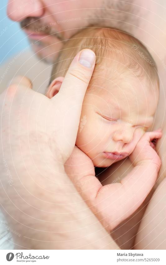 Mature father holding his sweet newborn baby. The baby sleeping in the arms of the father. dad skin-to-skin contact infant fatherhood parenting mature safety