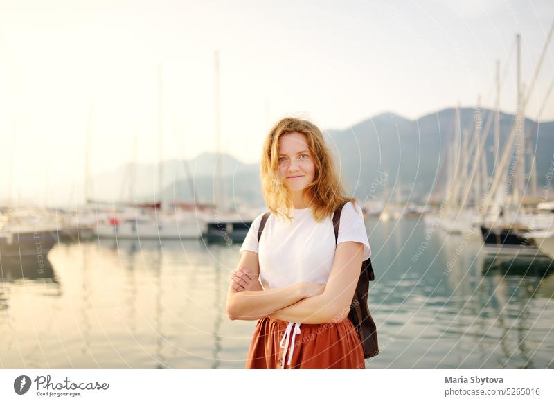 Charming young tourist woman travel by Mediterranean coast. Attractive red-haired girl on the background of sea and yachts. Yacht rental. Tourism and travel